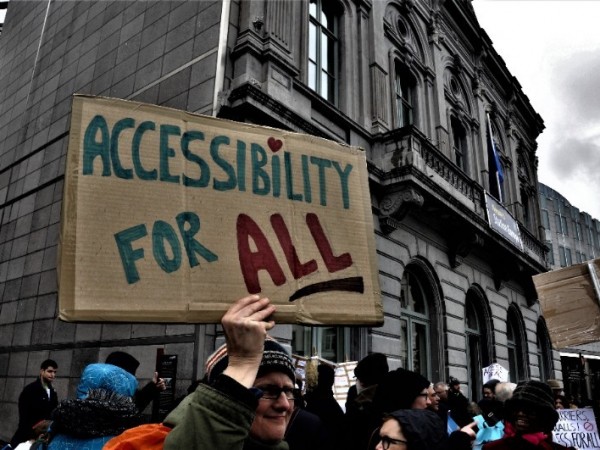 Φωτογραφία από διαδήλωση στις Βρυξέλλες για την προσβασιμότητα- διαδηλωτής κρατάει αυτοσχέδιο πλακάτ που αναγράφει "Accessiblity for All", Προσβασιμότητα για όλους