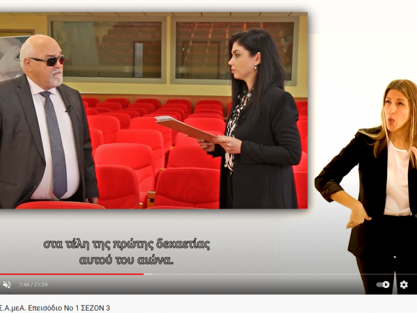 Ο Ι. Βαρδακαστάνης μιλά στην Νικολέτα Κανάκη, στη διερμηνεία Νοηματικής η Νεφέλη Ράντου, στο βάθος το αμφιθέατρο της ΕΣΑμεΑ